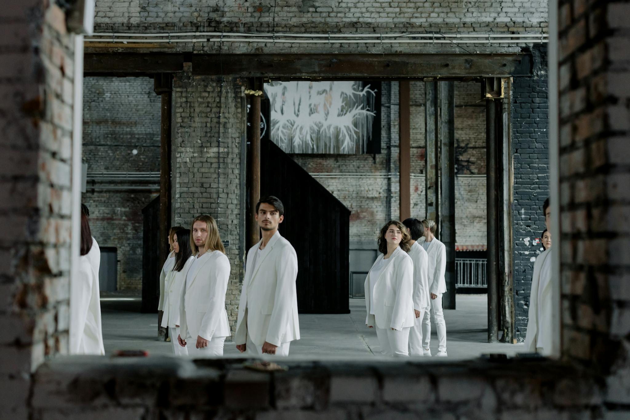 A diverse group of people in white clothes standing in an industrial setting with exposed brick and beams.