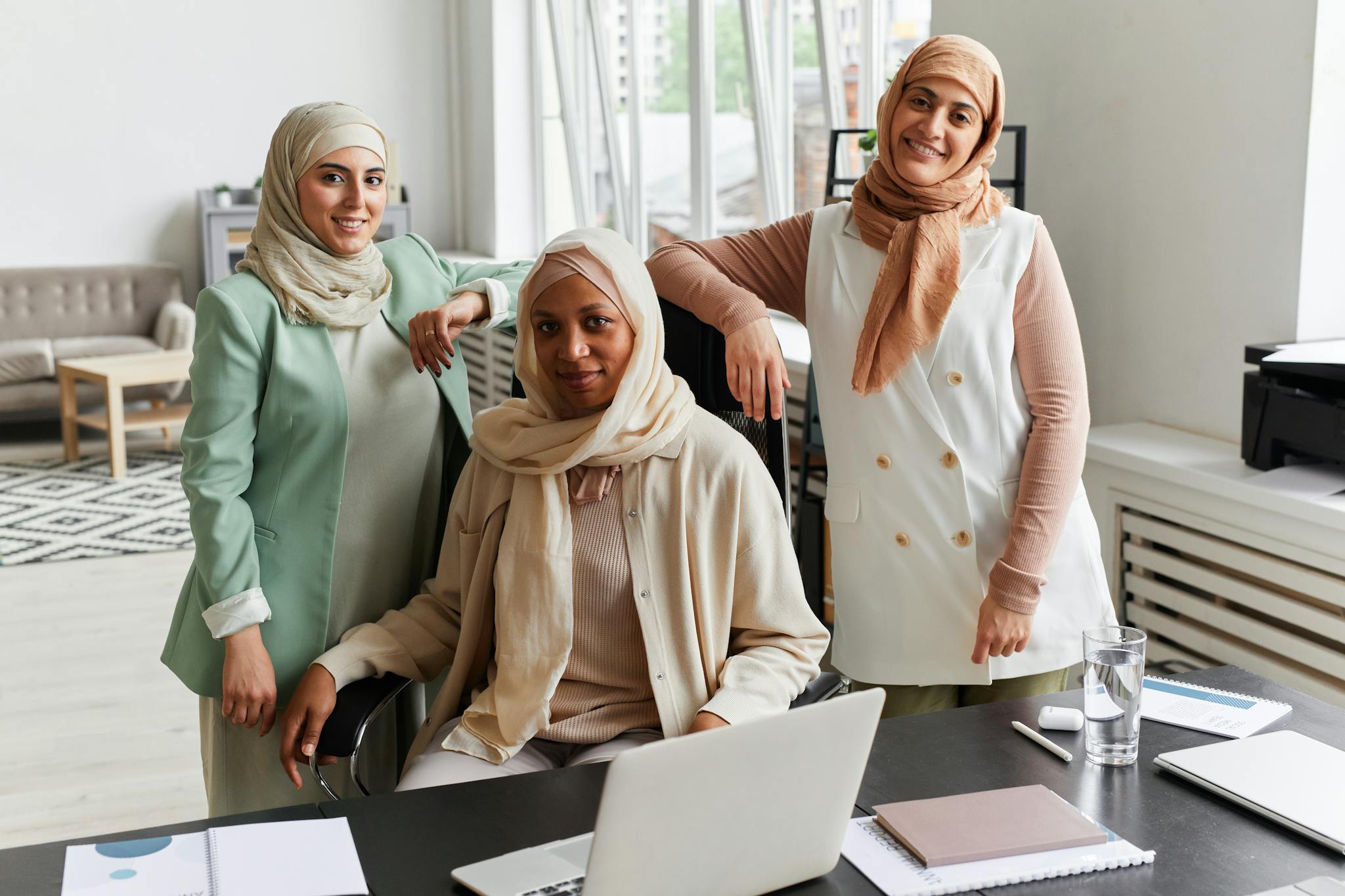 Three Muslim businesswomen in hijabs collaborating in a modern office setting.