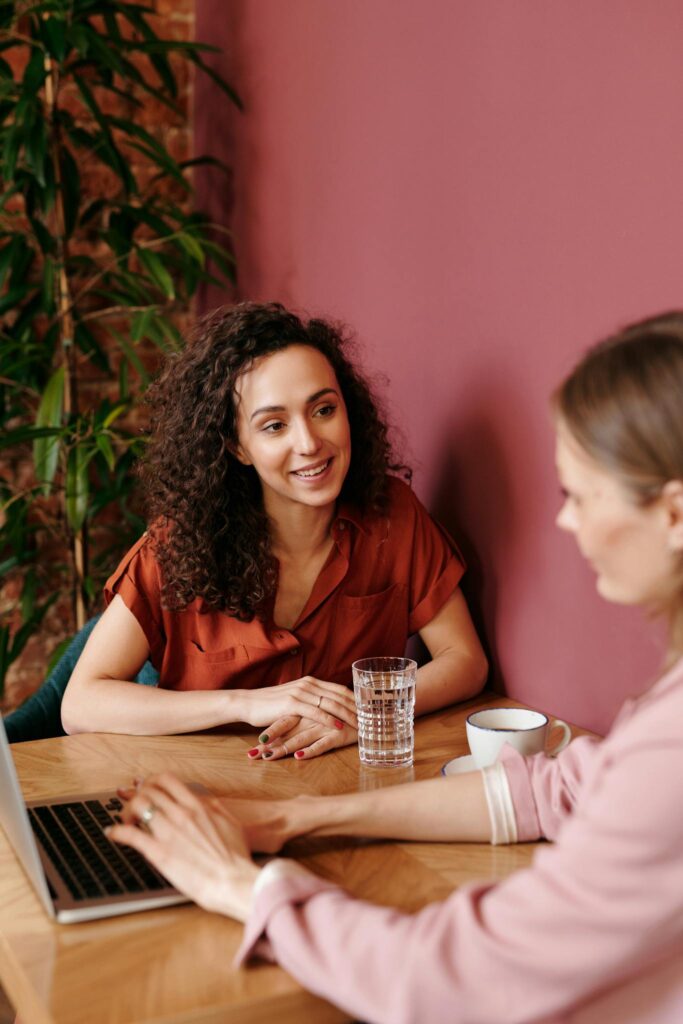 Two women engage in a collaborative discussion at a coffee shop table, sharing ideas and smiles.